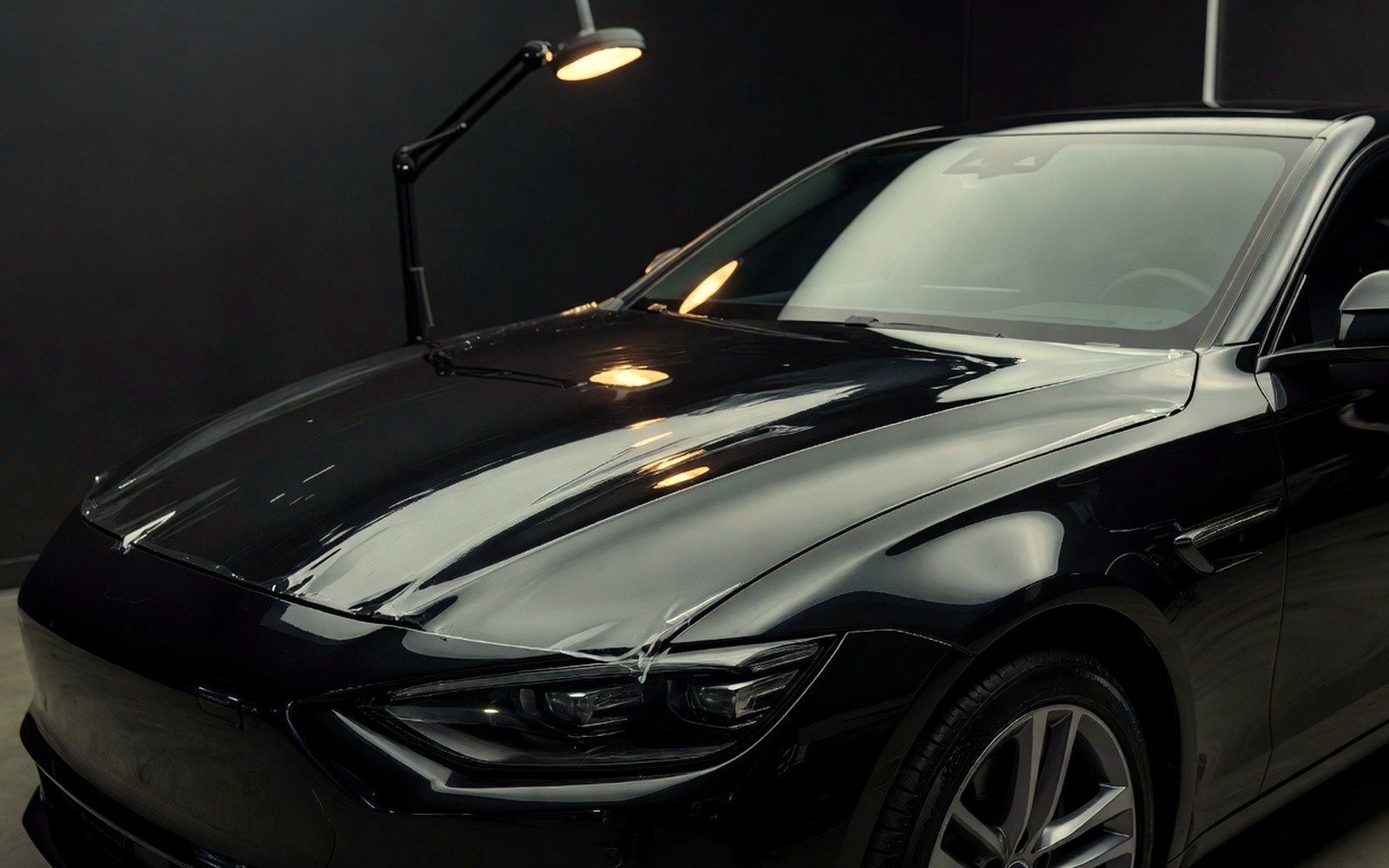 Glossy black vehicle hood and bumper protected with clear paint protection film under warm inspection light