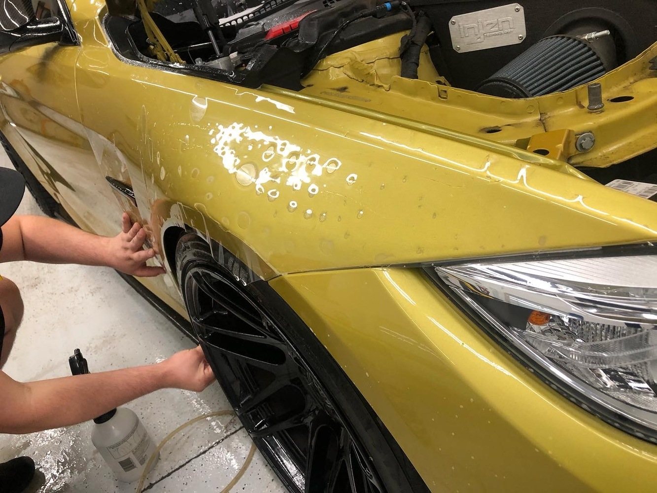 Installer positioning clear protection film on a yellow BMW front fender