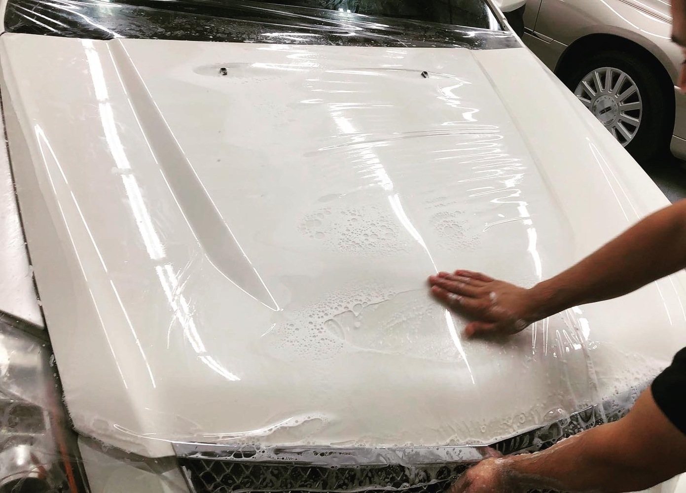 Clear paint-protection film being fitted over a white vehicle hood in the Chandler shop
